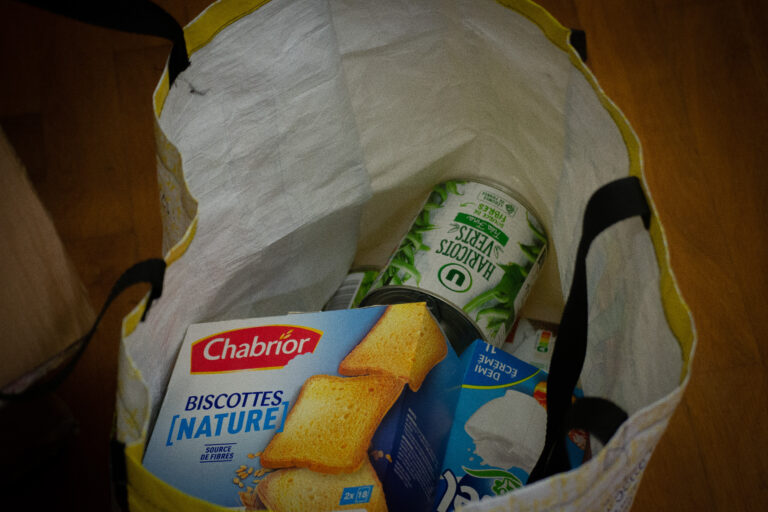 Un paquet de biscottes, une boîte de haricots et un sachet de riz sont dans le sac de courses d'un étudiant.