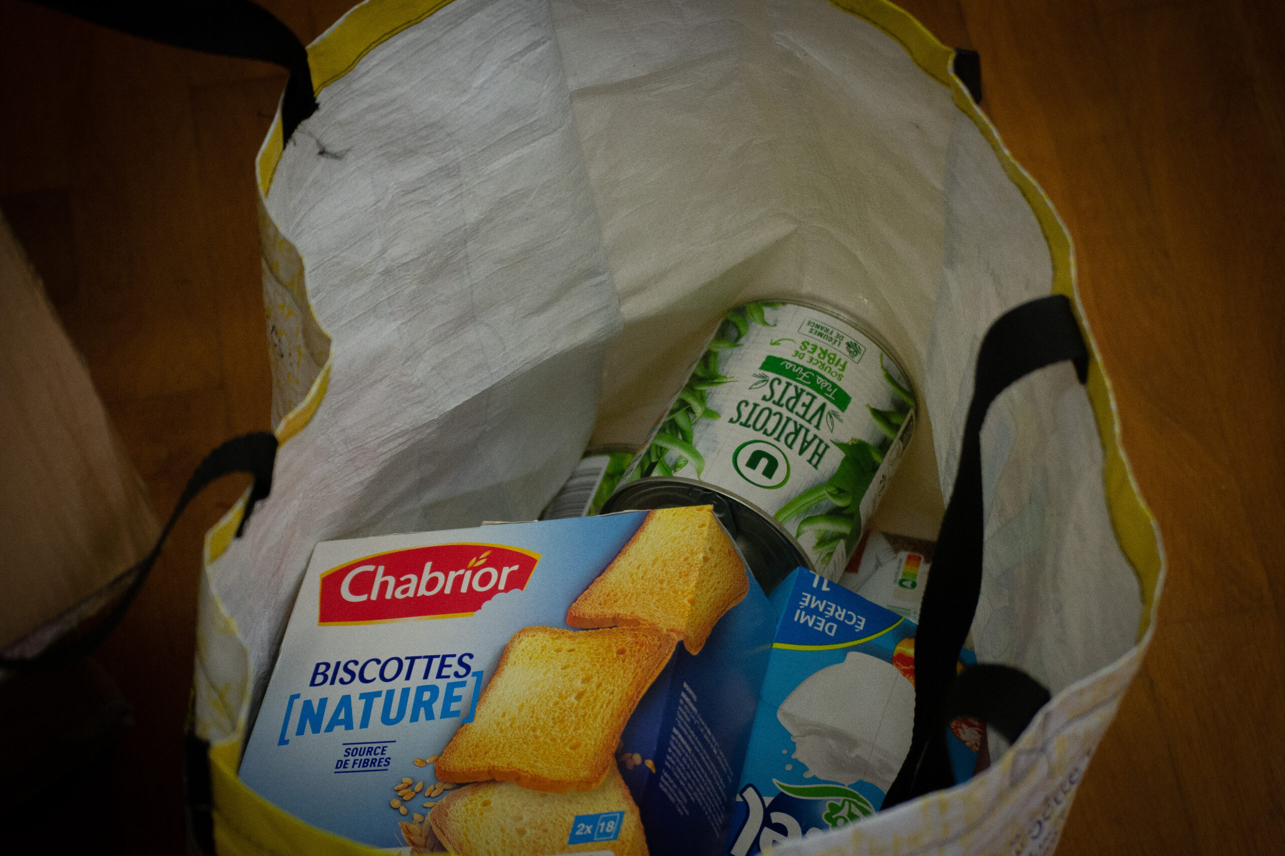 Un paquet de biscottes, une boîte de haricots et un sachet de riz sont dans le sac de courses d'un étudiant.