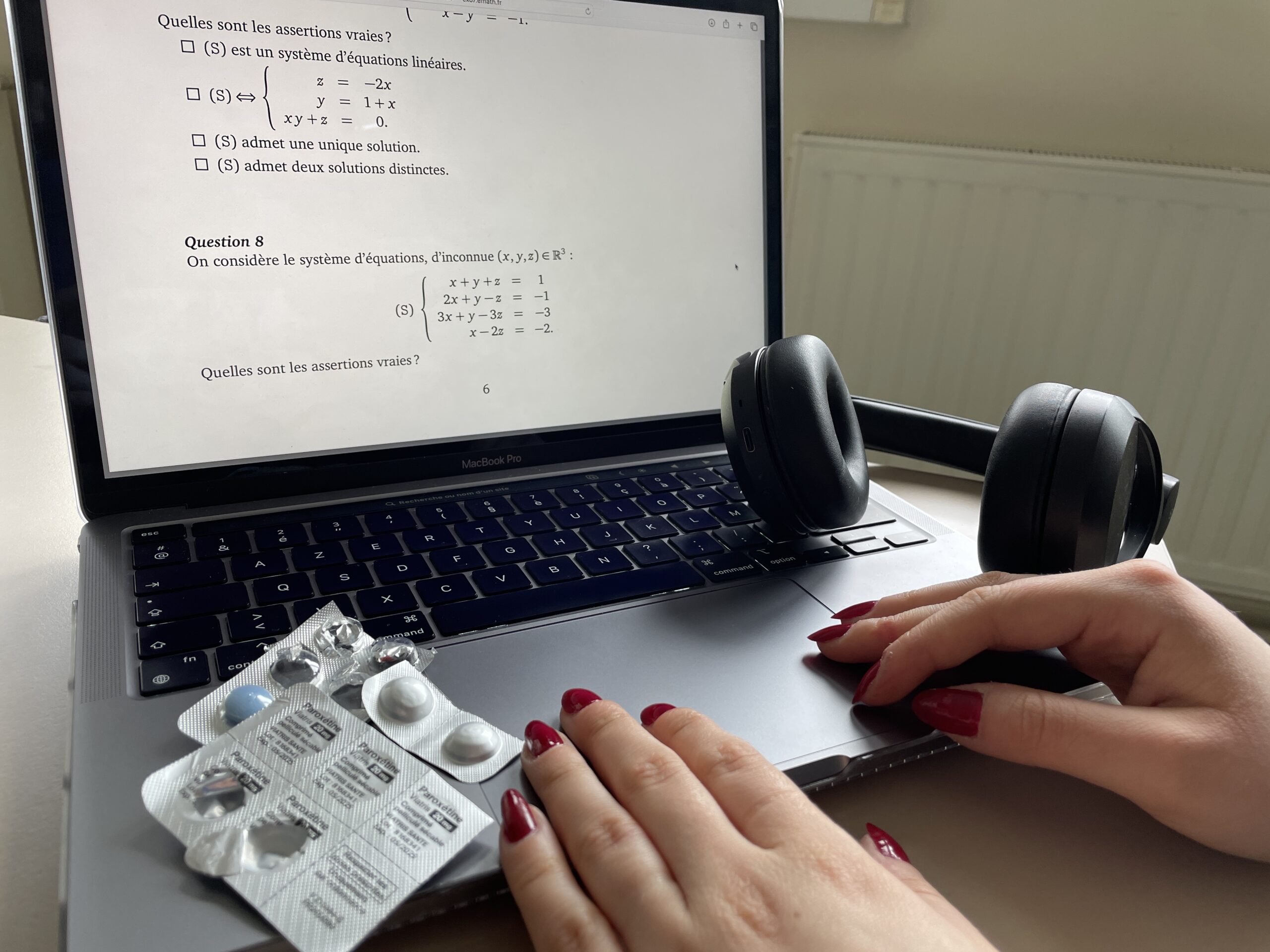 Des mains féminines sur un ordinateur, un casque audio et des antidépresseurs à côté.